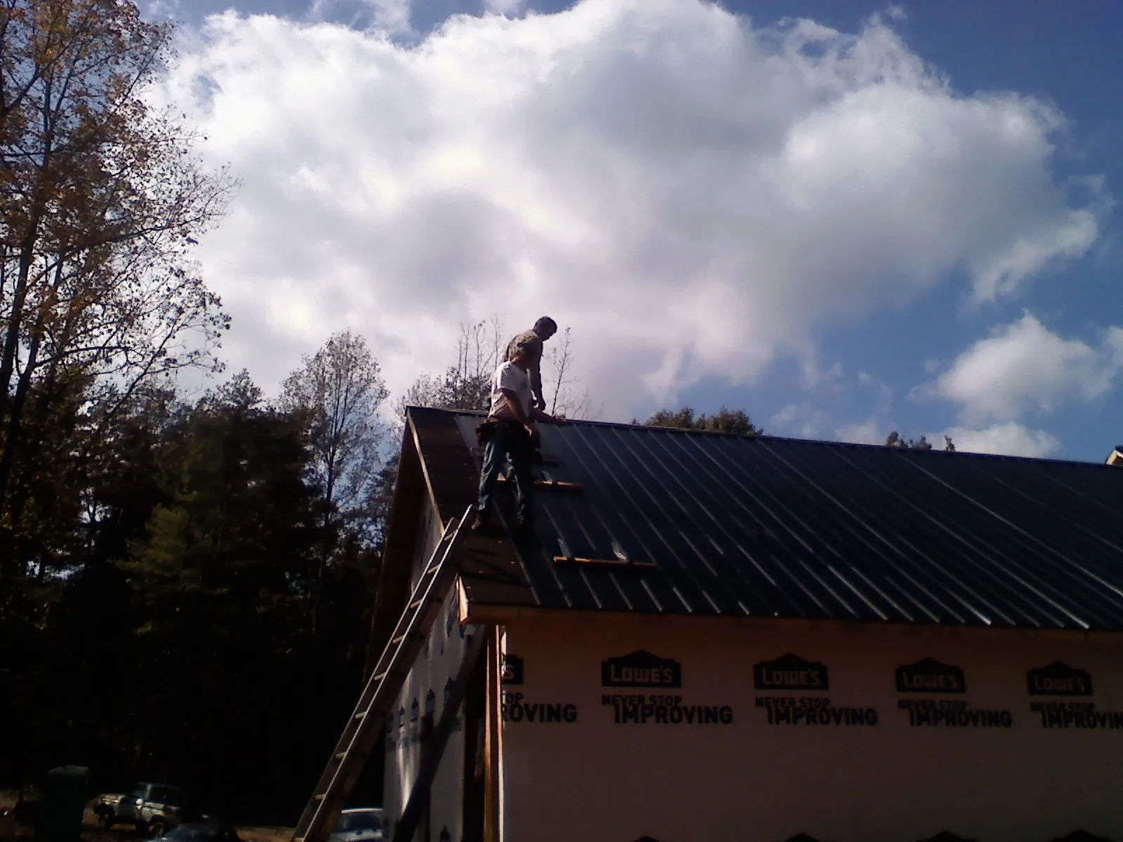 Roofer fastening dark metal panels high against a cloudy sky, from a Roof Inspection job in Salkum