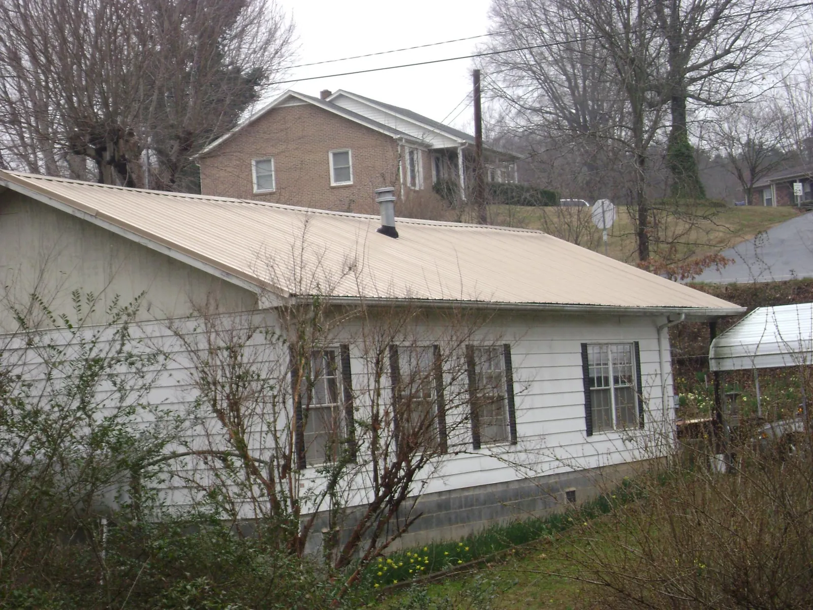 Tan metal roof on a white sided house set into a hillside — Commercial Roofing by Roofing Brothers in Salkum